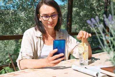 Woman blogging social media in smartphone during summer morning breakfast in cafe bar outdoors. 