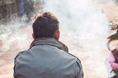 Rear view of man smoking while sitting outdoors