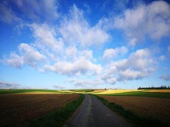 Empty road amidst fields against sky