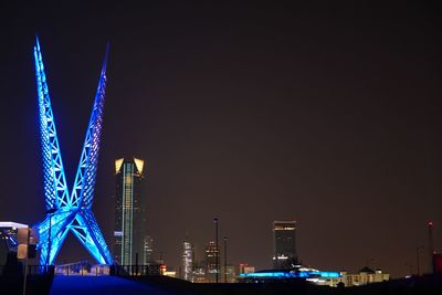 Illuminated ferris wheel in city against sky at night