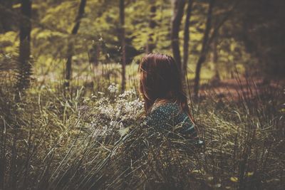 Rear view of woman sitting on field in forest