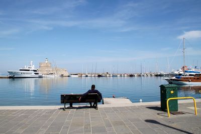 Man sitting on boat moored at harbor against sky