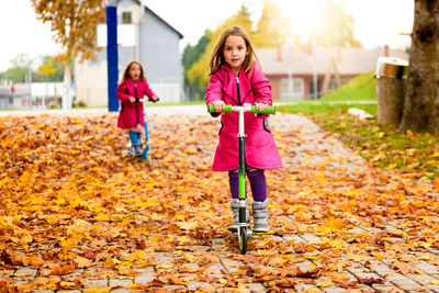 Girls riding push scooters at park during autumn