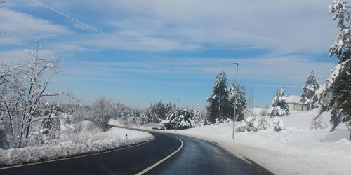 Road amidst trees against sky during winter