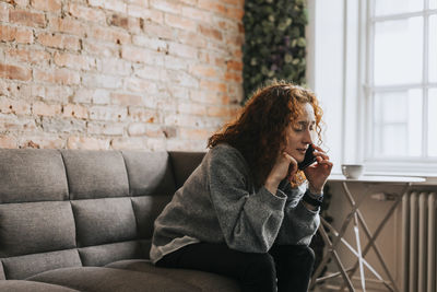 Redhead businesswoman talking on smart phone sitting on sofa at office