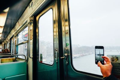 Cropped hand photographing eiffel tower through mobile phone while traveling in train