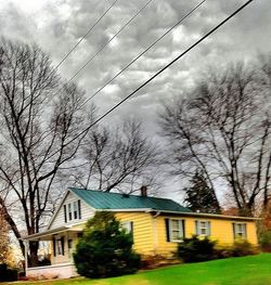 Houses and bare trees against cloudy sky
