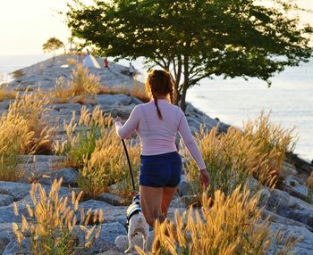 Rear view of woman with dog walking on groyne