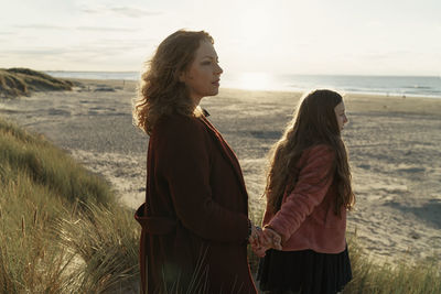 Woman with daughter standing on beach by sea against sky