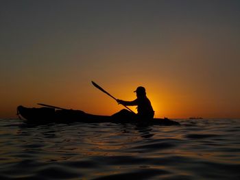 Silhouette person rowing boat in sea against clear sky during sunset