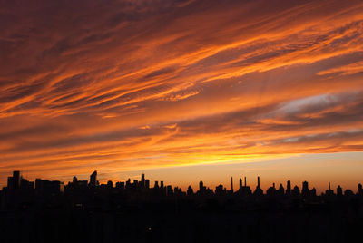 Silhouette buildings against dramatic sky during sunset