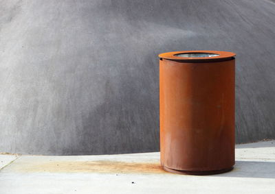 Old rusty metallic garbage bin against gray wall