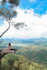 Full length of woman sitting on tree house against landscape
