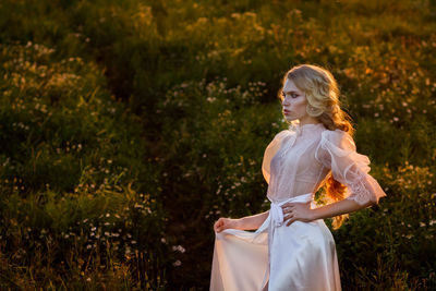 Beautiful young woman wearing white dress while standing on land at sunset