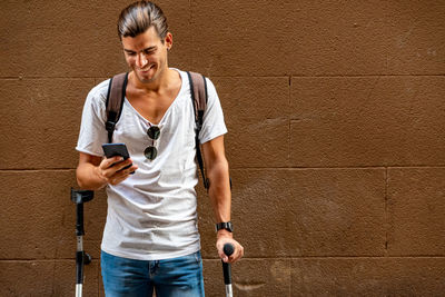 Young latin man with crutches and mobile in the street