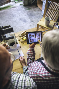 Portrait of man photographing with mobile phone while sitting on table