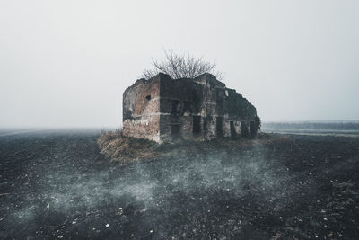 Abandoned building on field against sky during foggy weather