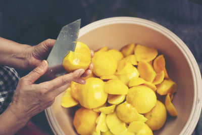 Cropped hands of person cutting mango fruit in container