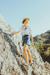 Low angle view of person standing on rock against sky