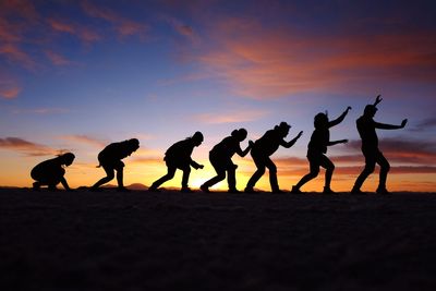 Silhouette people on sand at beach against sky during sunset