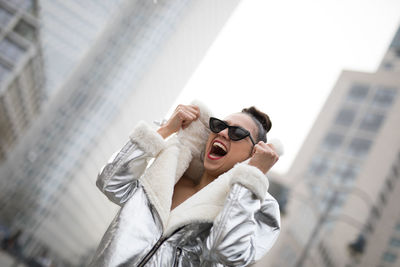 Low angle view of cheerful woman wearing warm clothing in city