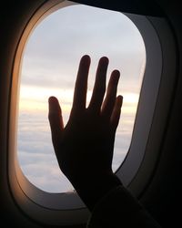 Cropped image of hand against sky seen through airplane window