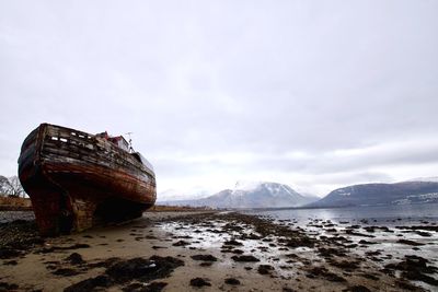 Abandoned boat on snow covered landscape against sky