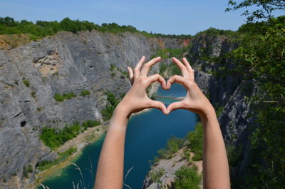 Cropped hands of woman making heart shape against mountains and sky