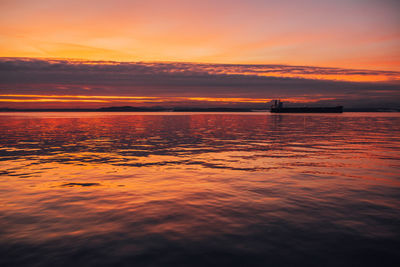 Pink, orange purple sunset over puget sound in seattle with barge, container ship in distance