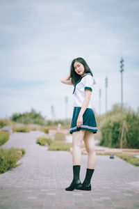 Portrait of woman standing on footpath against sky