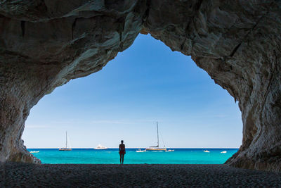 Rear view of woman standing in cave at beach against sea and sky
