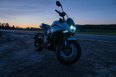 Motorcycle on road by field against sky during sunset