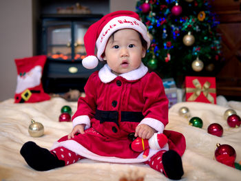 Portrait of cute baby girl wearing santa hat against christmas tree at home