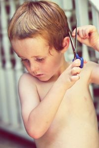 Close-up of shirtless boy cutting hair using scissors