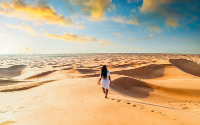 Rear view of woman walking at sandy beach