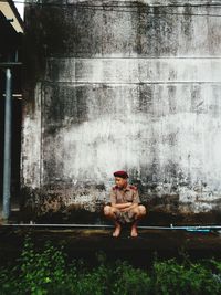 Full length of man sitting against wall