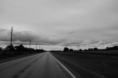 Country road amidst field against sky