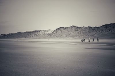 Mid distant view of men cycling at snow covered beach