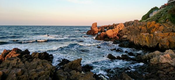 Rocks on shore by sea against sky