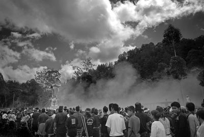 Rear view of people standing by trees against sky