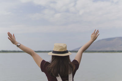 Rear view of woman with arms raised by sea against sky