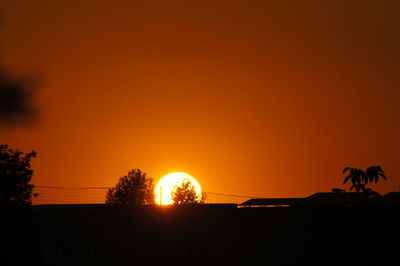 Silhouette trees on landscape against romantic sky at sunset