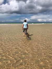 Rear view of woman walking with dog in sea at beach