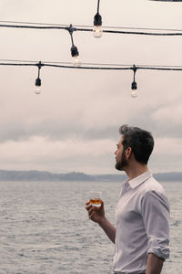 Man drinking alcohol in glass by sea against sky