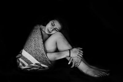 Woman hugging knees against black background