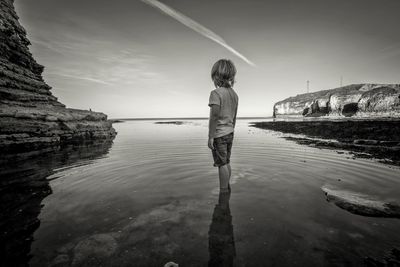 Full length of boy standing in water against sky