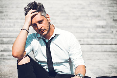 Portrait of sad man with hand in hair sitting on steps