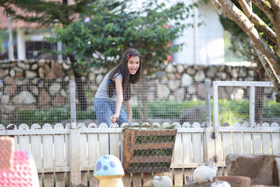 Cute girl standing by fence feeding rabbit 