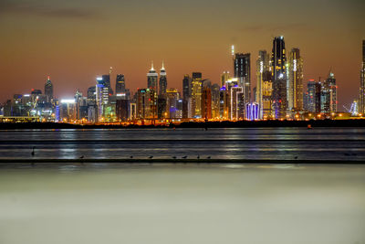 Illuminated city by river against sky at night