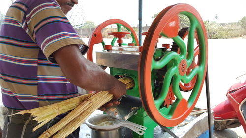 Midsection of vendor crushing sugar canes in machinery at market stall